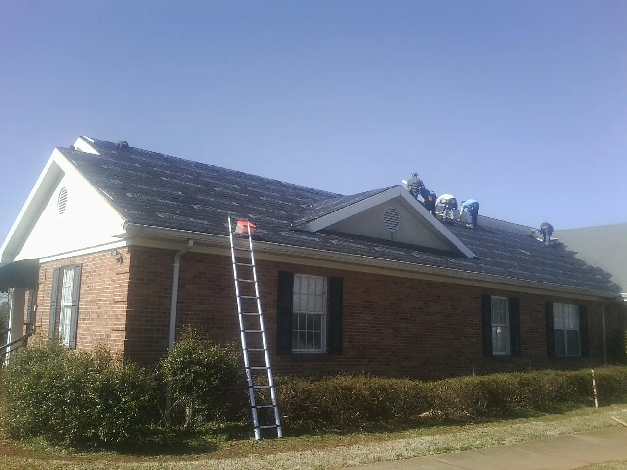 Crew tearing shingles off a brick ranch roof with a ladder set — Emergency Roof Repair work by our crew in Wakefield