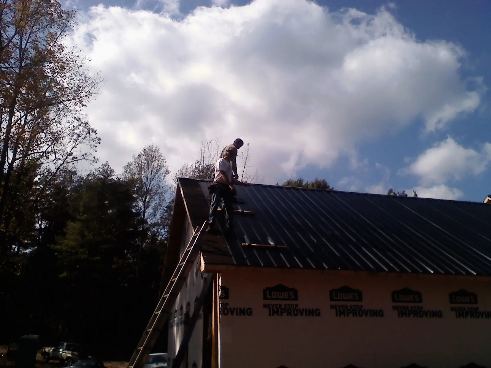 Roofer fastening dark metal panels high against a cloudy sky, from a Roof Inspection job in Wakefield